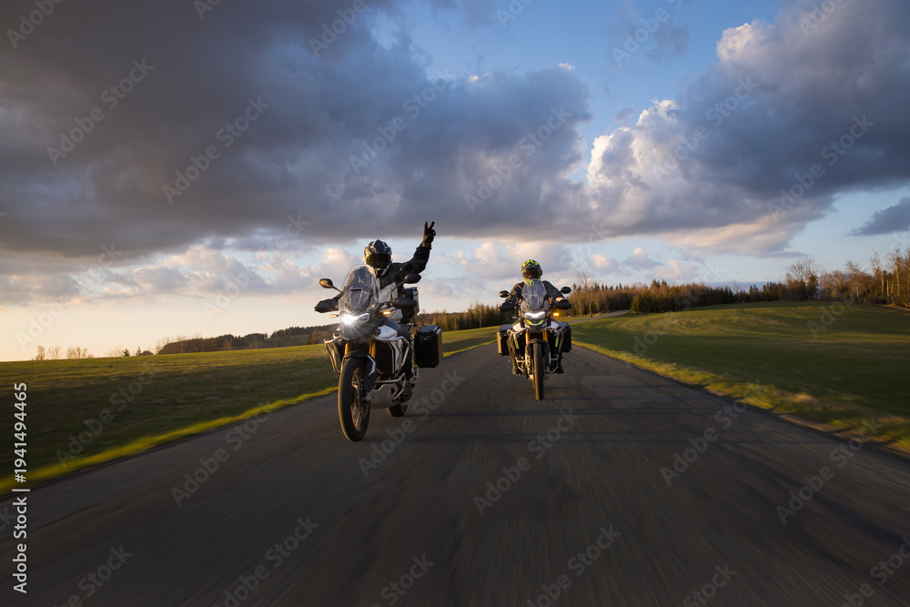 Fototapeta premium Drivers riding motorcycle on empty road during sunset, spring mountains