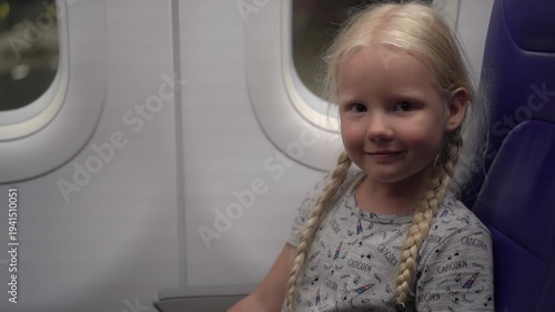 Happy child girl flying on an airplane and showing thumb up.