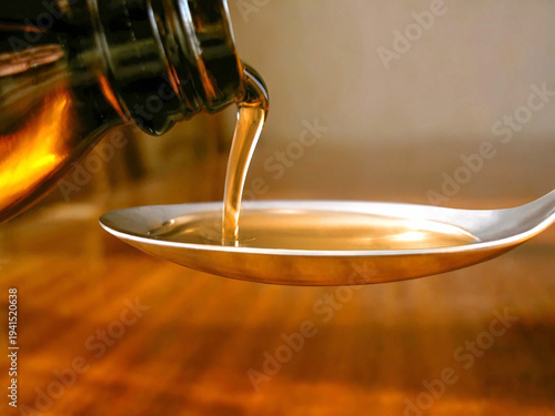 Quadro su tela Pouring golden oil or syrup onto a metal spoon, health and supplement concept