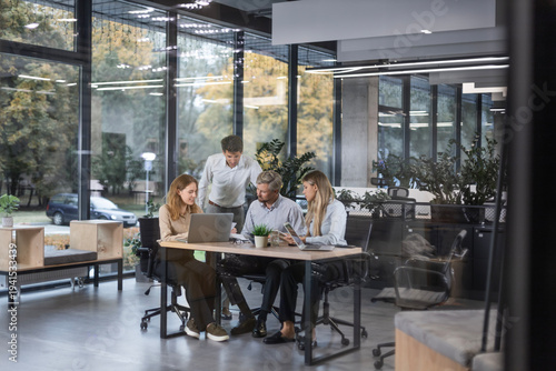 A modern office interior, featuring a blurred view of workers at desks, through a glass partition