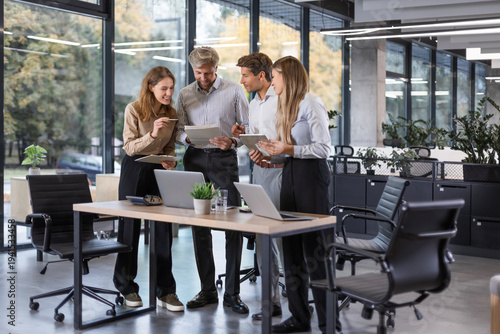 Business people discussing work together using a tablet and laptop taking notes in a modern office.