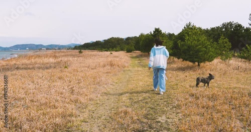 young woman and small dog  walking in the field on seashore