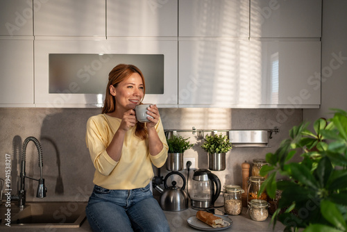 Fotografie Woman enjoying morning coffee in contemporary kitchen basking in sunlight