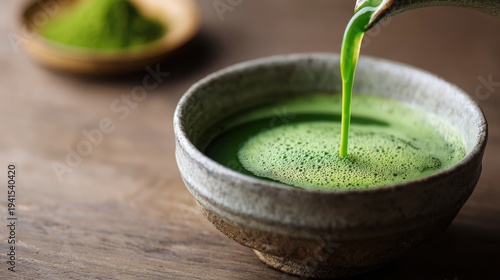 Vibrant green matcha latte artfully poured into a traditional ceramic bowl creating frothy foam, a refreshing and healthy beverage.