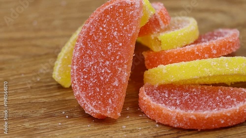 Close-up of sugar-coated lemon and orange jelly slices on a wooden table, rotating view.