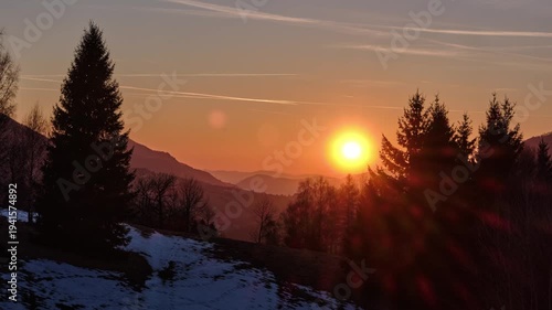 Timelapse of golden sunset over winter mountain landscape with silhouettes of spruce trees