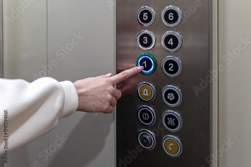 Hand Pressing First Floor Elevator Button. Close-up of a woman pressing the first floor button inside an elevator, showing modern lift controls, transportation access, and building interior.