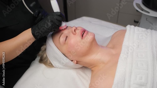 Professional cosmetologist performing a radiofrequency lifting facial treatment on a female client
