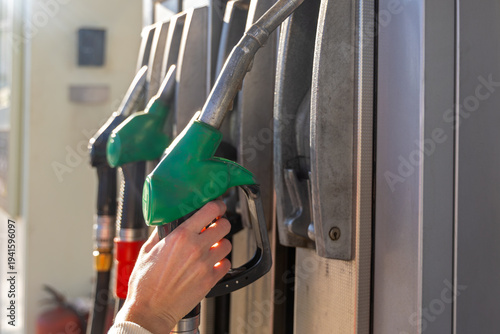 Hand Removing Green Gas Pump Nozzle. Close-up of a hand taking a green fuel nozzle from a gas station pump, showing refueling equipment, energy supply, and transport service.