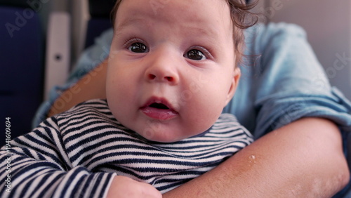 Fotografie Baby gazing up in mother’s arms on train, close-up of innocent expression, wide-