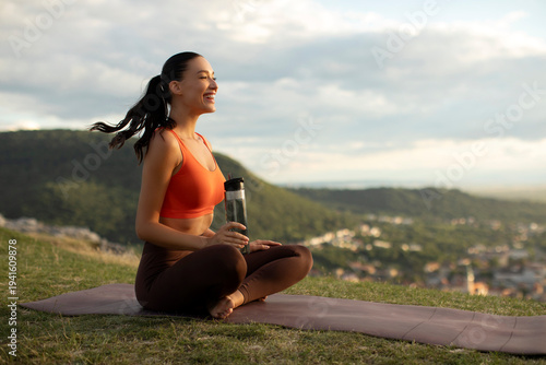 Foto Satisfied woman sitting on yoga mat in the mountains, holding water bottle and s