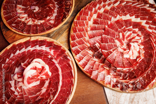Three wooden trays of sliced Spanish jamon ham on a table