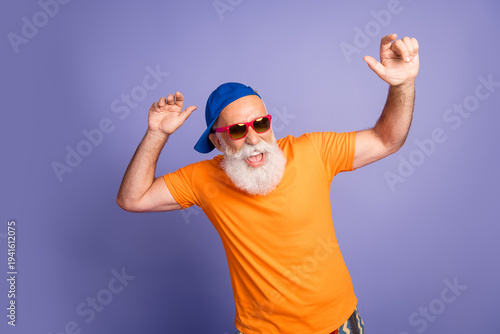 Εκτύπωση καμβά Playful senior man in orange t‑shirt dances with arms raised against purple back