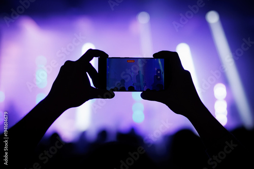 Person recording a live concert with smartphone in a purple lit arena