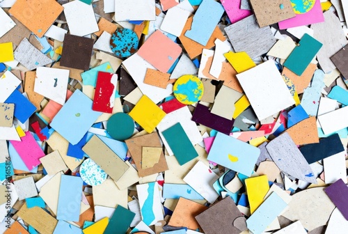 Scattered colorful painted rectangular and circular tile or foam pieces on light surface.