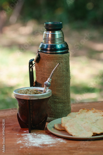 Slika na platnu Mate y Termo de acero sobre mesa rústica de madera, de fondo plantas y pasto