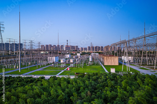 High-voltage electrical substation and power transmission infrastructure integrated with urban landscape at dusk.