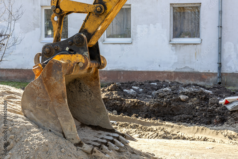 Fototapeta premium Excavator bucket digging trench during urban construction and infrastructure repair