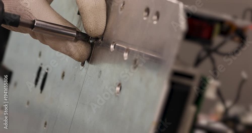 Close-up of a technician using a screwdriver to remove screws from a metal panel. Industrial maintenance and repair process with protective gloves, demonstrating technical work, assembly and disassemb