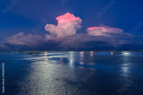 Fotografía Vast wet asphalt ground reflecting bright lights under a dramatic evening sky with glowing pink clouds