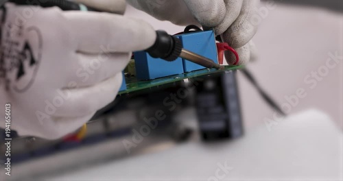 Technician connecting electrical wires to a terminal using a screwdriver. Close-up of hands in protective gloves performing electrical installation or equipment maintenance on an electronic device.
