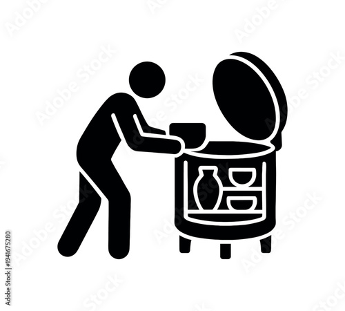 Solid black silhouette of a person putting a pot or bowl into a round kiln or oven with the lid open.