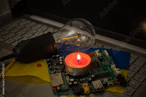 Energy crisis in Ukraine: candlelight on motherboard and laptop with ukrainian flag