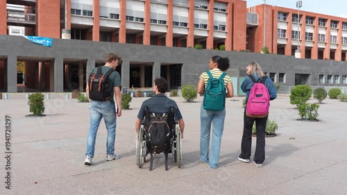 Rear view of a diverse group of college students walking together in a university courtyard. One student is in a wheelchair
