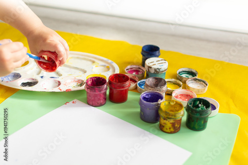 Child's hands drawing on white paper with colorful gouache, copy space, kid's education