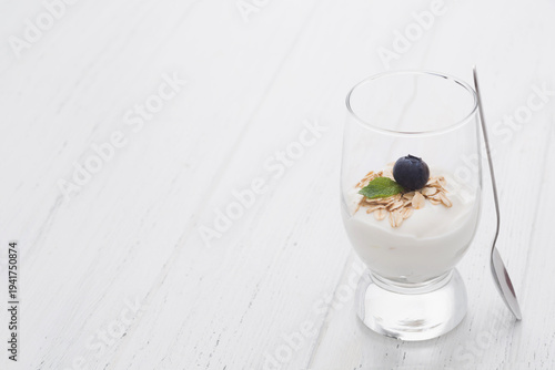 Greek yogurt with oatmeal and blueberry in glasses with spoon over white wooden background with copy space