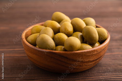 Fresh green olives in wooden bowl on brown wooden. side view, close up, selective focus