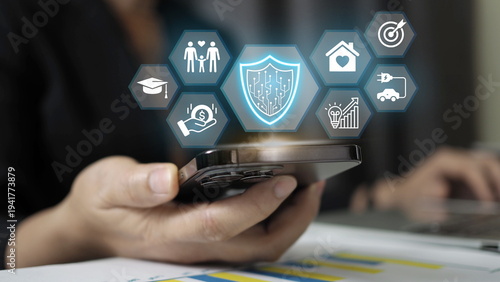 Business professional holding smartphone with digital protection shield and insurance service icons. Concept of cybersecurity, digital protection, insurance technology, financial security 
