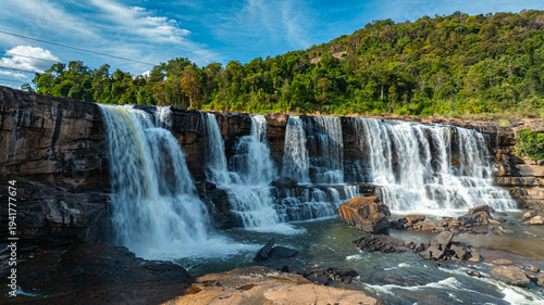Aerial view of Sae Pong Lai Waterfall reveals a tropical river cascading over layered rock formations, surrounded by lush green forest and untouched wilderness.
