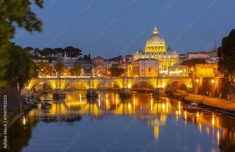 Fototapeta premium Night view of Saint Peter Basilica and bridge over the Tiber river in Rome with golden lights reflecting in calm water.