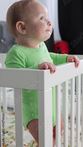 Young Baby Gazes In Peaceful Nursery. Adorable Infant In Softlit Room Exhibits Wonder While Gripping Crib Railing Confidently vertical video