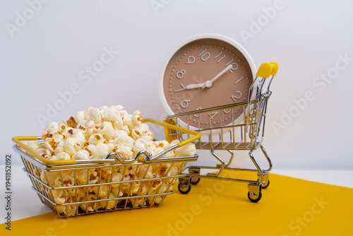 Alarm clock with measuring tape in shopping cart full of popcorn. Time management for healthy eating. 