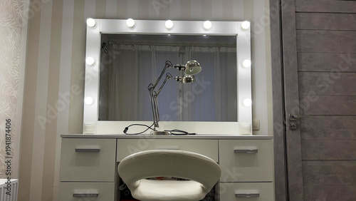 Lighted dressing mirror with bulbs and a metal desk lamp on a vanity table, clean minimalist home studio setup