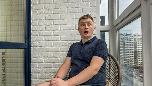 Canvas Print Surprised man on an apartment balcony with city buildings behind, shocked reacti