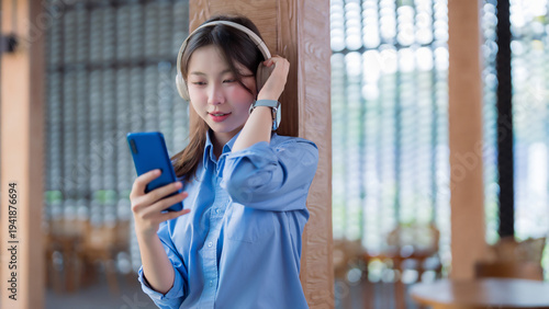 Asian young adult woman enjoying music podcast audiobook via headphones smartphone modern cafe lounge technology leisure digital content relax