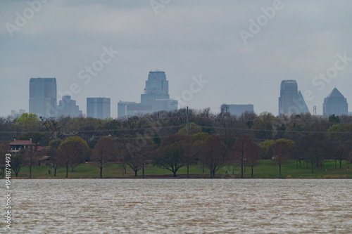 Skyscrapers and buildings making up parto the the Dallas, Texas skyline rising boe the trees on the shore of White Rock Lake.