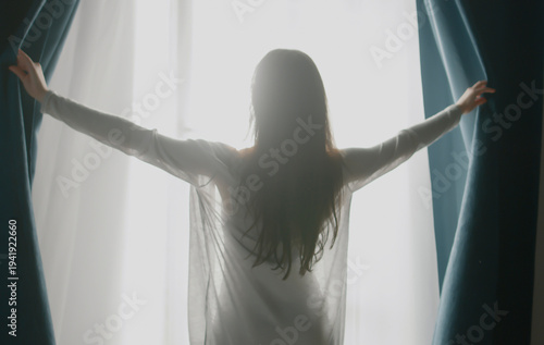 Back rear view confident woman in night robe gown pulling opening lace curtains after waking up in morning, admiring panorama view near big window,enjoying start of new day at home