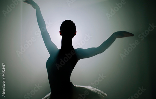 Ballerina in black tutu dress dancing on stage with magic blue light and smoke. Silhouette of young attractive dancer in ballet shoes pointe performing in dark. Copy space.