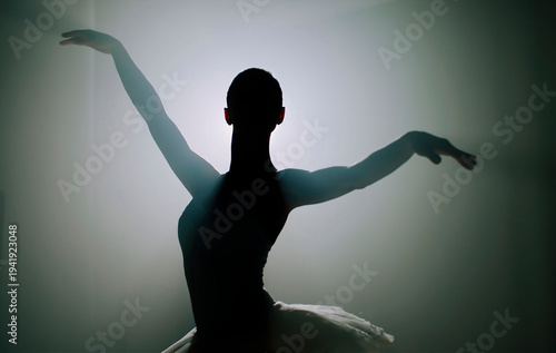 Ballerina in black tutu dress dancing on stage with magic blue light and smoke. Silhouette of young attractive dancer in ballet shoes pointe performing in dark. Copy space.