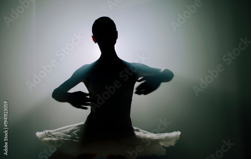Ballerina in black tutu dress dancing on stage with magic blue light and smoke. Silhouette of young attractive dancer in ballet shoes pointe performing in dark. Copy space.