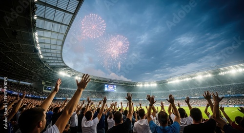 A large crowd of spectators cheering at a sports stadium with fireworks exploding overhead.