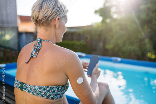 Woman using smartphone with wearable health sensor on arm.