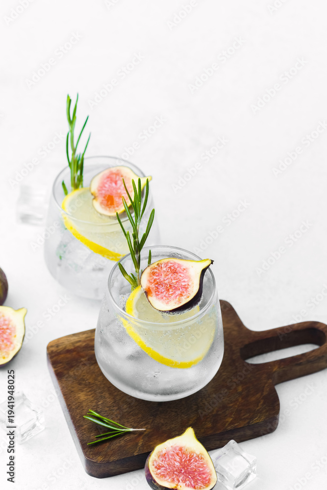 Naklejka premium Two lemon cocktails with fig rosemary and ice served in glasses on wooden board with fruit and herb decoration