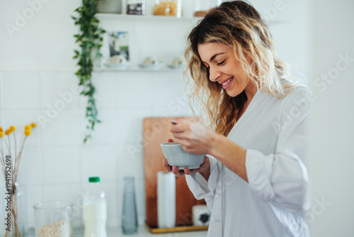 Tableau sur toile Blonde woman smiling while making breakfast in a bright home kitchen enjoying a
