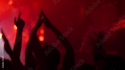 Dynamic video showing a silhouetted crowd raising hands and applauding at a vibrant live music concert or club party. Energetic atmosphere with flashing red stage lights creating a captivating visual