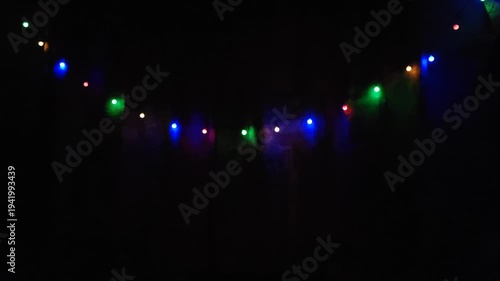 A garland of bright colorful lights hanging in a dark room. Playful glow and cozy decorative atmosphere
